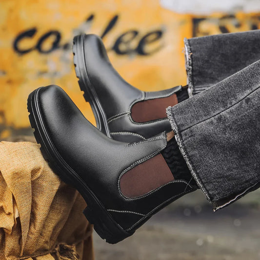 Black Chelsea boots with brown elastic side panels worn with grey jeans in a café setting