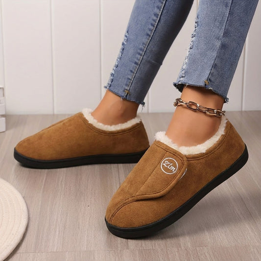 Tan fleece-lined adjustable slippers with front flaps, worn indoors on a wooden floor