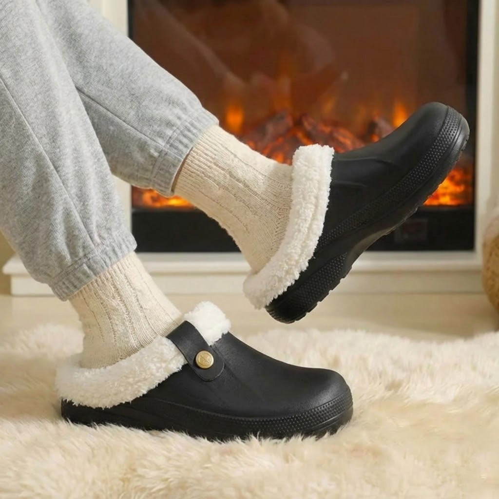 Black fleece-cuff winter clogs worn with cream socks beside a fireplace