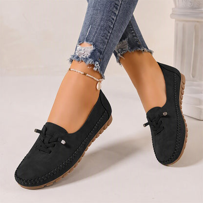 Black women's suede slip-on loafers with rounded toes, angled view on feet